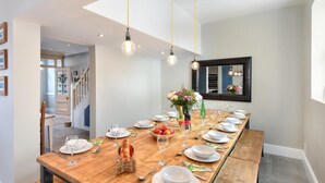 A long wooden dining table set with white plates, glasses, and cutlery, a basket of bread, and a vase with flowers.