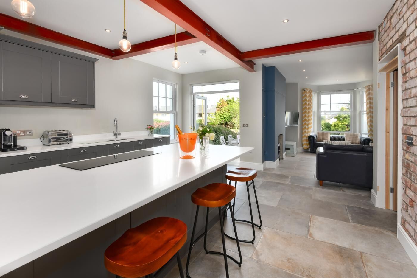 Een moderne keuken met een groot eiland, grijze kastjes en een accentmuur van baksteen.