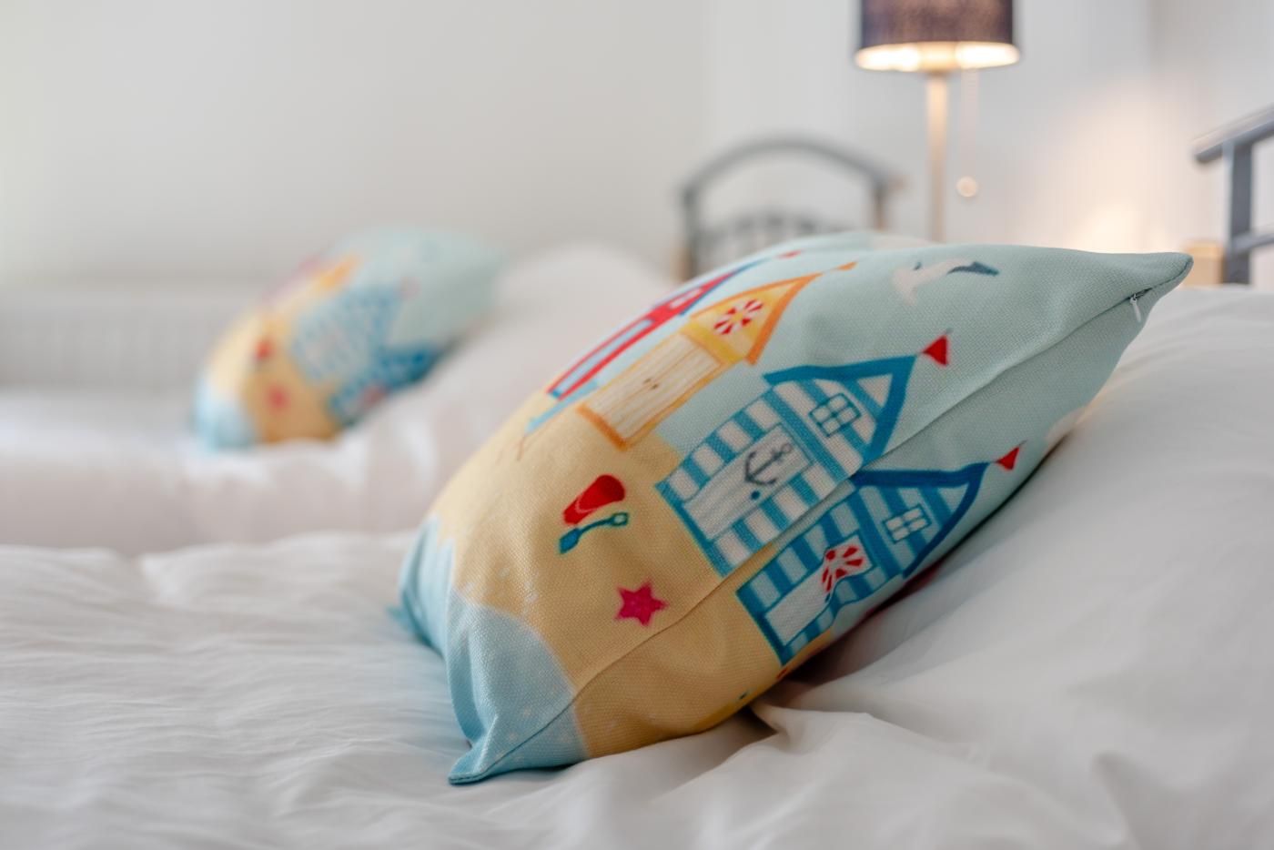 A bed with white bedding and colorful pillows featuring house and star patterns.