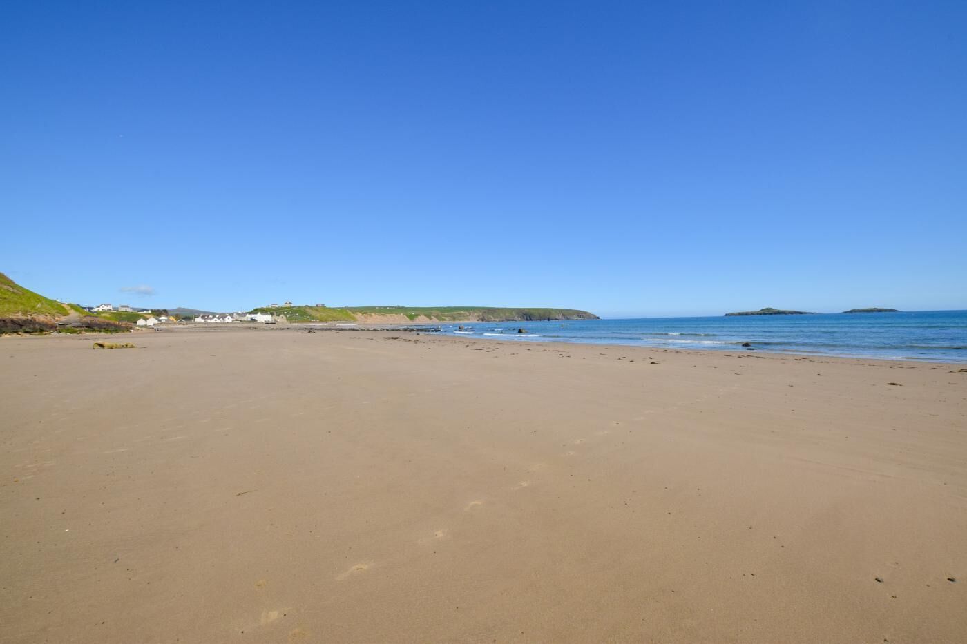 Ein weiter Sandstrand mit blauem Himmel, ruhigem Meer und Hügeln in der Ferne.