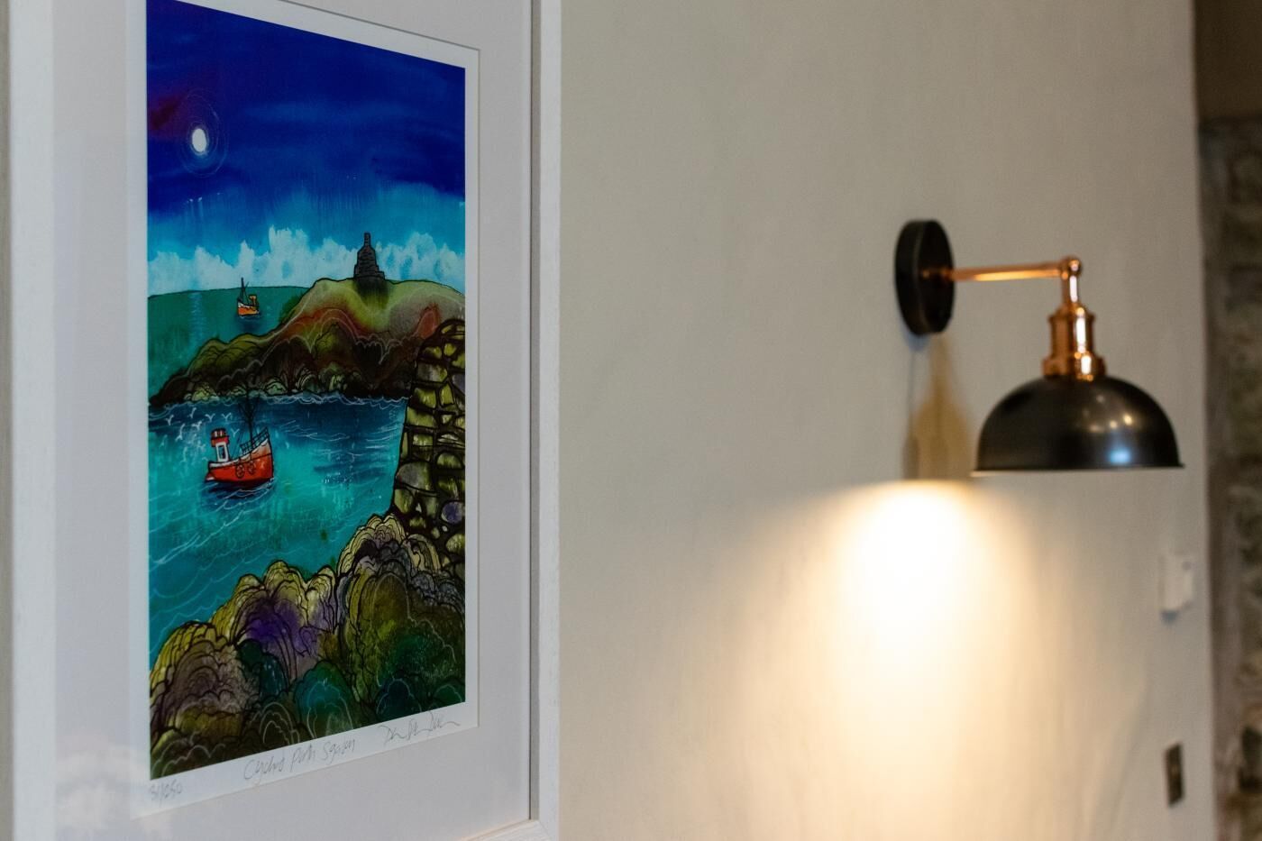 Une œuvre d’art encadrée représentant un paysage côtier avec un bateau, un phare et un ciel illuminé par la lune.