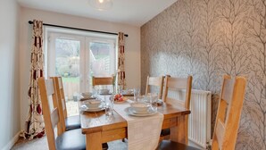 Un coin repas avec une table en bois dressée pour quatre personnes, des chaises, un radiateur et une fenêtre avec des rideaux.