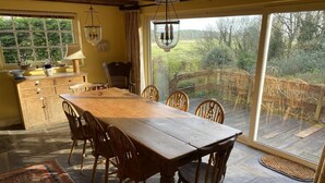 A dining area with a wooden table and chairs, a large window, and a view of the outdoors. - 5 Bed in Llanmadoc (oc-hh2111) (Llanmadoc)