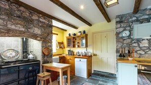 A kitchen with a stone wall, wooden cabinets, a wooden table, and a tiled backsplash. - 5 Bed in Llanmadoc (oc-hh2111) (Llanmadoc)