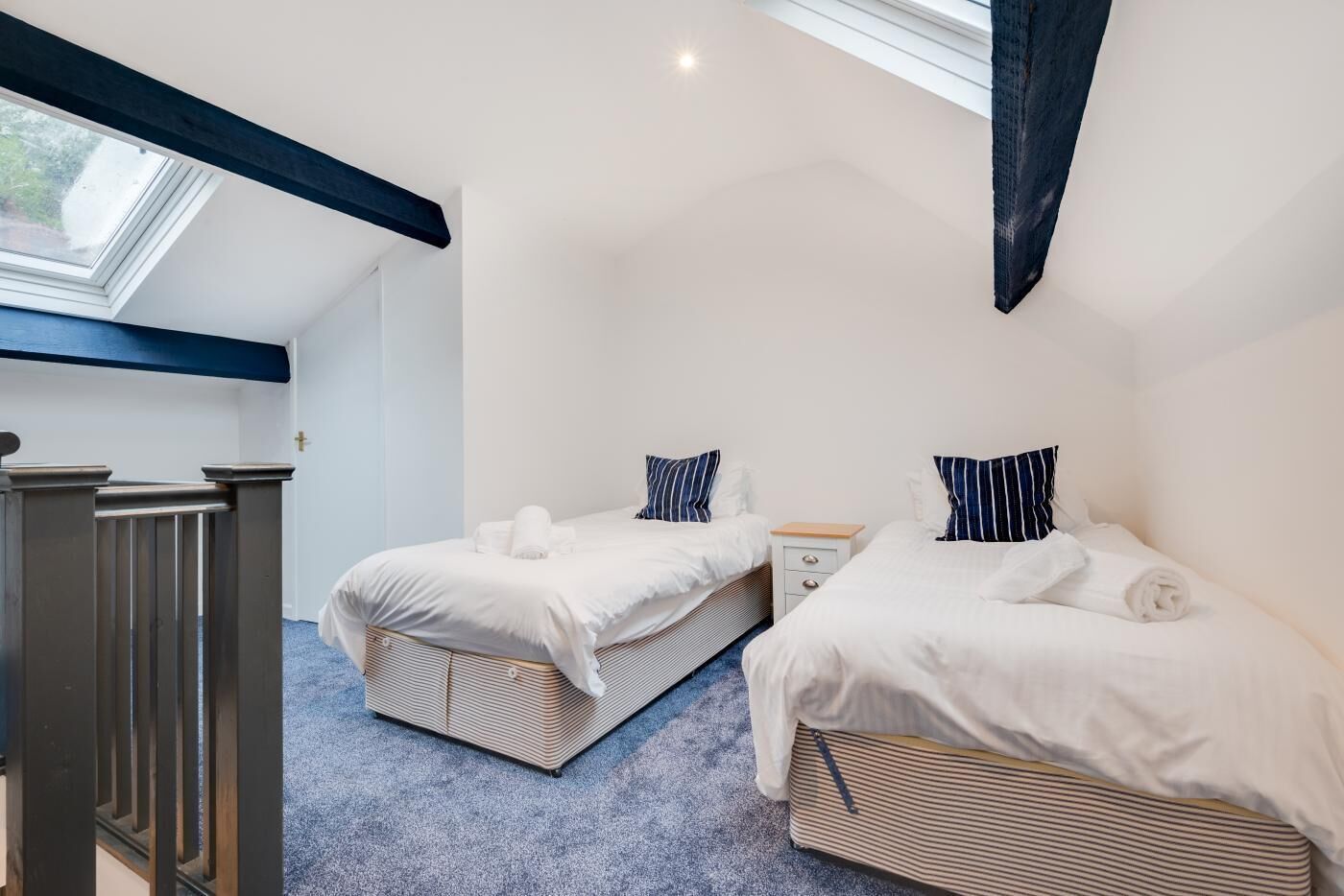 A bedroom with two single beds, a small bedside table, a window, and a skylight.