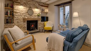 A cozy living room with a stone wall, a fireplace, a yellow chair, a blue sofa, and a bookshelf. - 3 Bed in Fowey (oc-p00871) (Fowey)