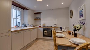 A modern kitchen with a wooden dining table set for four, a built-in oven, and a window providing natural light. - 3 Bed in Fowey (oc-p00871) (Fowey)
