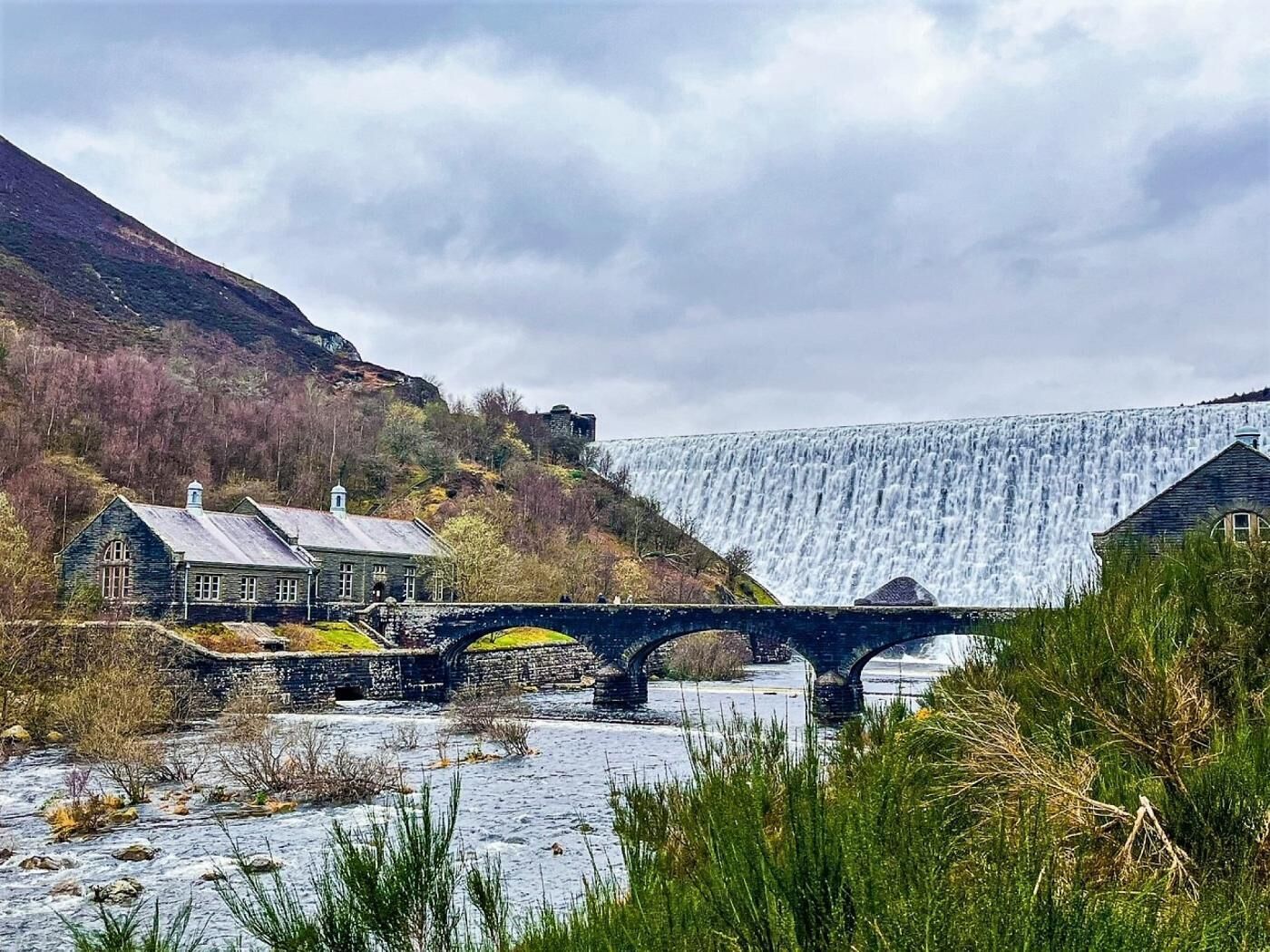 Een brug over een rivier met een waterval op de achtergrond.
