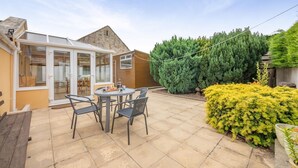 A patio with a table and chairs, a conservatory, and a large green hedge. - 2 Bed in Lowick (oc-414296) (Lowick)