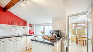 A modern kitchen with white cabinetry, a red accent wall, and a dining area with a view. - 2 Bed in Lowick (oc-414296) (Lowick)