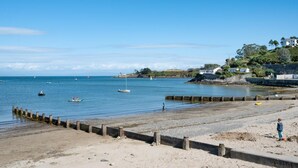 Une plage avec une jetée en bois, une mer calme, des bateaux et un enfant qui joue.