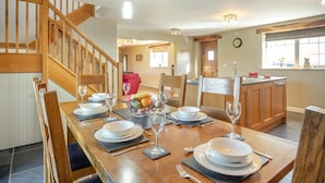 Un comedor con una mesa de madera dispuesta para cuatro, una cocina al fondo y una escalera que sube a un nivel superior.