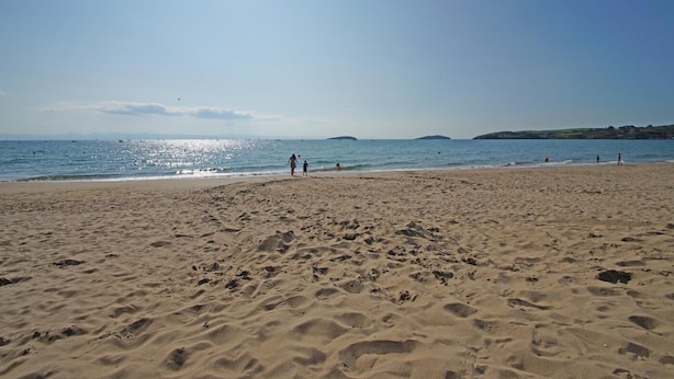 Una playa arenosa con huellas, cielo despejado y mar tranquilo.