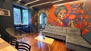 Indretning i en hyggelig café med sofa, stole, et lille bord og et muralmaleri på væggen.