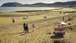 A beach with people walking and sitting, a colorful beach umbrella, and a view of the sea and hills in the background. - 1 Bed in Conwy (oc-bow118) (Conwy)