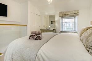 Quarto com cama, mesa de cabeceira, espelho, janela com cortinas e televisão na parede.
