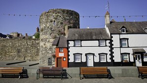 A stone tower, a white building with black trim, and a bench in a sunny outdoor setting. - 1 Bed in Conwy (oc-bow118) (Conwy)