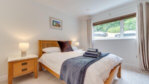 Een slaapkamer met een houten bed, twee nachtkastjes, een raam met gordijnen, en een ingelijst beeld aan de muur.