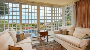 A spacious living room with a large bay window, a beige sofa, a wooden chair, and a patterned rug. - 4 Bed in Abersoch (oc-trefab) (Abersoch)