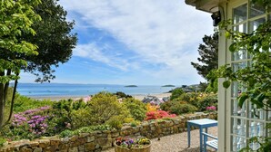 A garden with a stone wall, a wooden barrel planter, and a view of the beach and sea. - 4 Bed in Abersoch (oc-trefab) (Abersoch)
