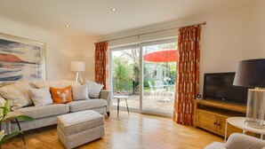 Een woonkamer met een bank, een poef, een televisie en een eethoek met stoelen en een tafel.