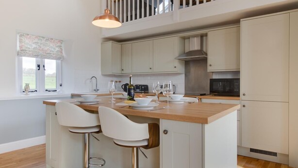 A modern kitchen with a central island, white bar stools, and a dining area.
