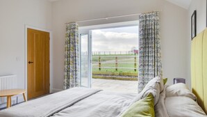A bedroom with a bed, a wooden door, and a view of a grassy area through a glass door.