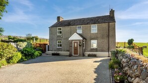 Une maison à deux étages avec une allée en gravier et un mur de pierre sur le côté droit.