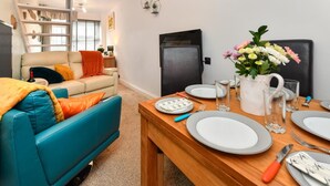 A modern living room with a sofa, a dining table set for four, and a kitchen area with a refrigerator. - 2 Bed in Nefyn (oc-tynixs) (Nefyn)