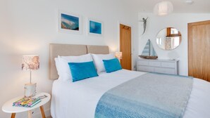 Een slaapkamer met een bed, bedlampjes, een dressoir, een spiegel en kunstwerken aan de wanden.
