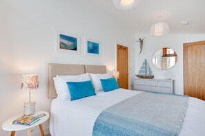 A bedroom with a bed, bedside lamps, a dresser, a mirror, and artwork on the walls. - 2 Bed in Polruan (oc-p00896) (England)
