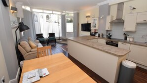 Eine moderne Küche mit einer zentralen Kochinsel, ein Essbereich mit Tisch und Stühlen sowie ein Wohnbereich mit Sofa und Sesseln.