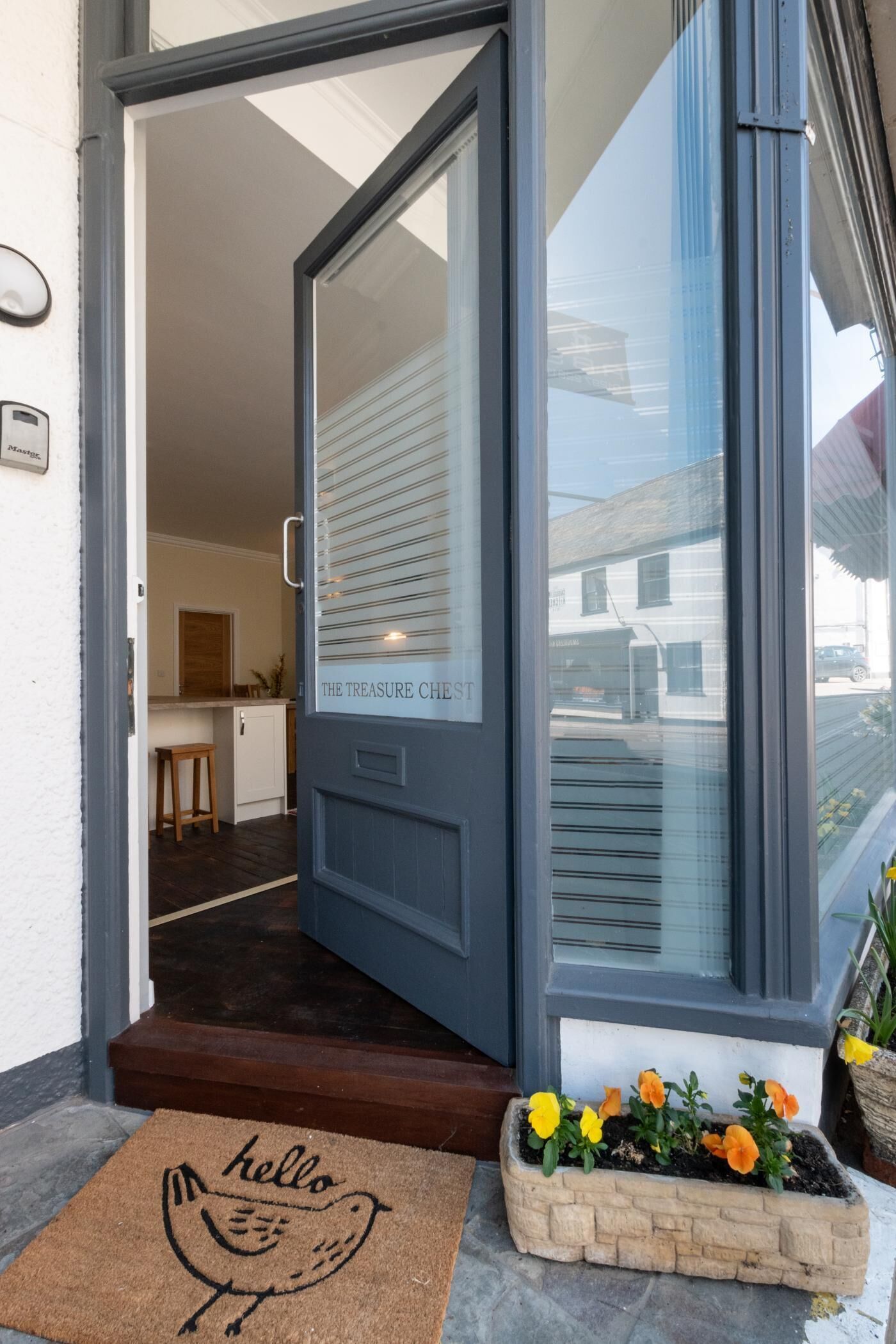 A door with a 'hello' doormat and a flower bed outside.