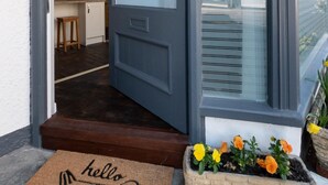 Eine Tür mit einer Fußmatte mit dem Schriftzug 'hello' und einem Blumenbeet davor.