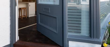 Une porte avec un paillasson sur lequel est écrit « bonjour » et un parterre de fleurs à l’extérieur.