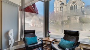 Ein Zimmer mit zwei Ledersesseln, einem kleinen Tisch und Blick auf eine Kirche durch große Fenster.