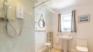 Ein Badezimmer mit Dusche, Toilette, Waschbecken und einem kleinen Hocker.