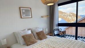 Une chambre à coucher avec un grand lit, une table de chevet, une chaise et une fenêtre donnant sur un paysage enneigé.
