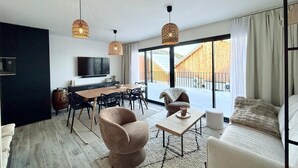 Un salon moderne comprenant un canapé, un fauteuil, une table basse et un coin repas avec des chaises et un téléviseur.