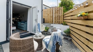 A modern outdoor living area with wicker furniture, a covered table, and a wooden fence. - 1 Bed in Porthleven (oc-portb) (Porthleven)