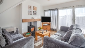 Ein modernes Wohnzimmer mit Kamin, grauen Sofas, einem Holztisch und einem Flachbildfernseher auf einem Holzständer.