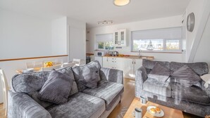 Ein modernes Wohnzimmer mit zwei grauen Sofas, einem Holztisch und einem Essbereich mit weißem Tisch und Stühlen.
