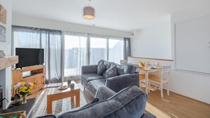 Ein modernes Wohnzimmer mit grauem Sofa, einer Holz-Unterhaltungseinheit und einem Essbereich mit weißem Tisch und Stühlen.