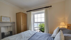 A bedroom with a bed, a wooden wardrobe, a window with curtains, and a lamp. - 4 Bed in New Quay (oc-bow272) (New Quay)