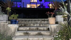 Een huis met een opvallend driehoekig dak, een veranda met treden en potplanten aan weerszijden.