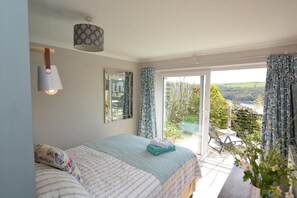 Une chambre à coucher comprenant un lit, une lampe de chevet, un miroir et une vue sur l’extérieur grâce à une porte coulissante.