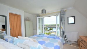 Een slaapkamer met een bed, een dressoir, een kledingkast en uitzicht op het omliggende landschap.