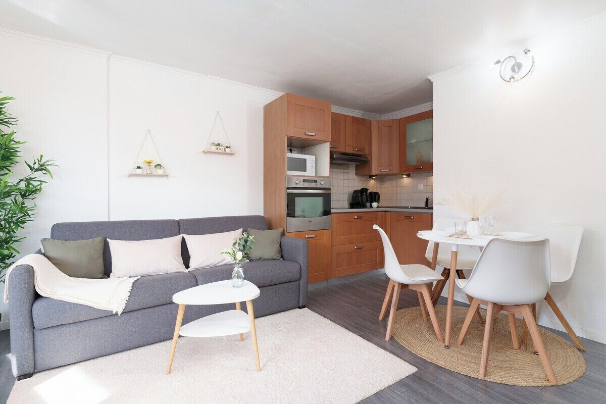 A modern living room with a grey sofa, white coffee table, and a dining area with white chairs and a small table.