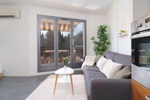 A modern living room with a grey sofa, a small white table, and a large sliding glass door leading to an outdoor deck. - The Cozy : Terrace • Parking • Pool • A/C (Grasse)
