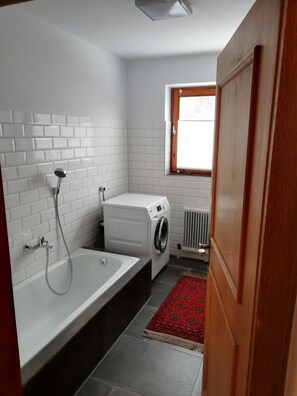 Een kleine badkamer met een bad, een wasmachine en een radiator.
